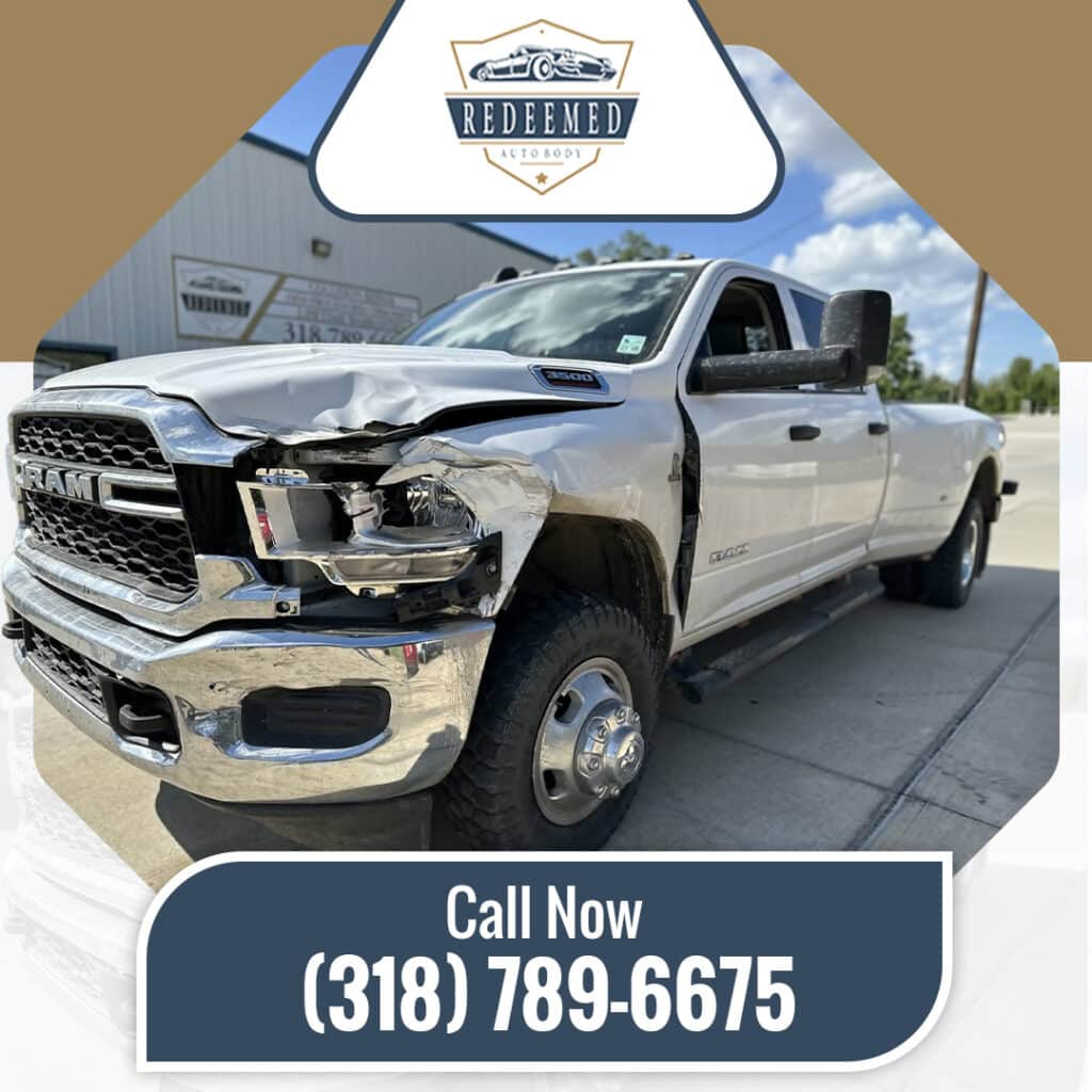 A white Ram 3500 pickup truck with severe front-end driver side collision and fender damage parked outside an auto body shop.