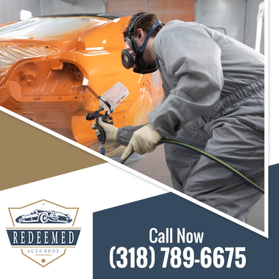 Certified auto body technician wearing a respirator and paint suit applying bright orange paint to a car quarter panel with a spray gun.